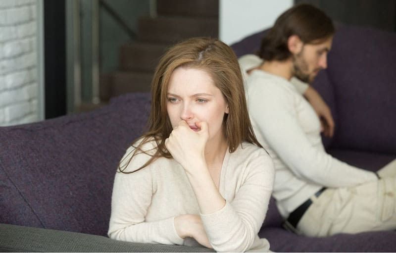 traurige enttäuschte frau, die auf dem sofa denkt und sitzt, weit entfernt von einem mann, der auf demselben sofa sitzt
