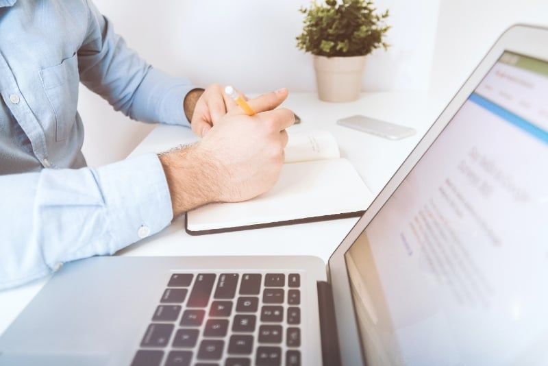 bărbat care scrie în notebook lângă laptop