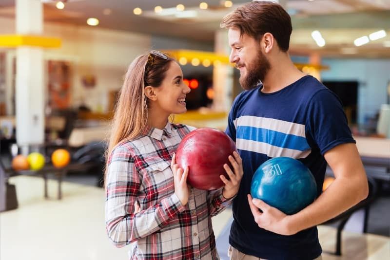 pria dan wanita melakukan kontak mata sambil memegang bola bowling