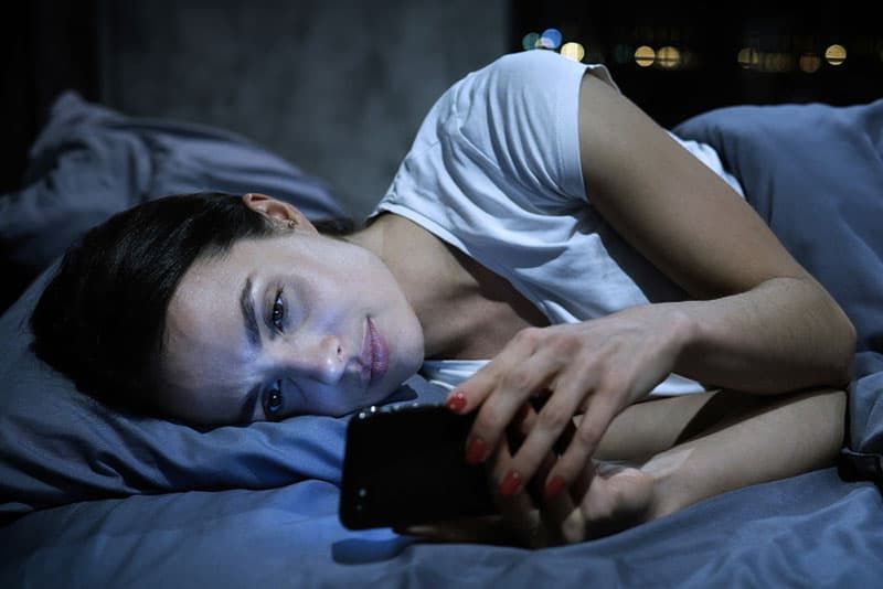 dona trista mirant el telèfon al llit