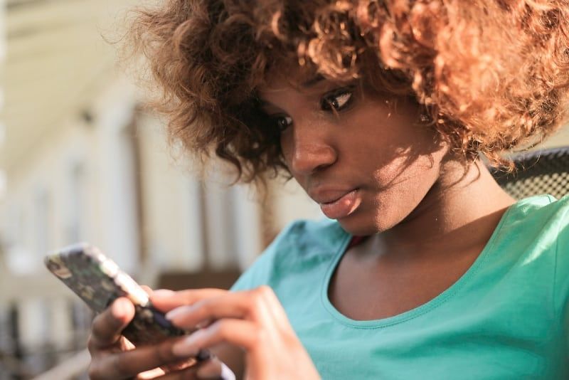 ženska s kodrastimi lasmi, ki uporablja pametni telefon na prostem