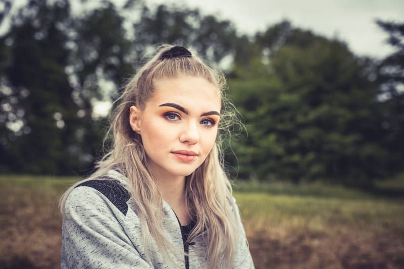 blondinka v sivi majici s kapuco sedi na prostem