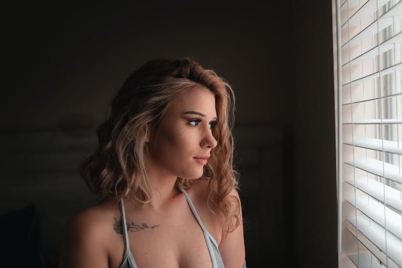 femeie blondă cu tatuaj care se uită prin fereastră