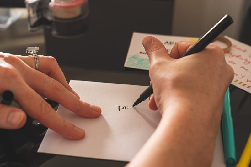 kobieta pisze na białym papierze siedząc przy stole