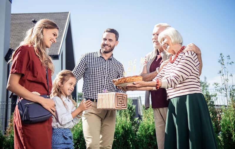 família jove feliç visitant els seus parents madurs portant regals reunint-se a l