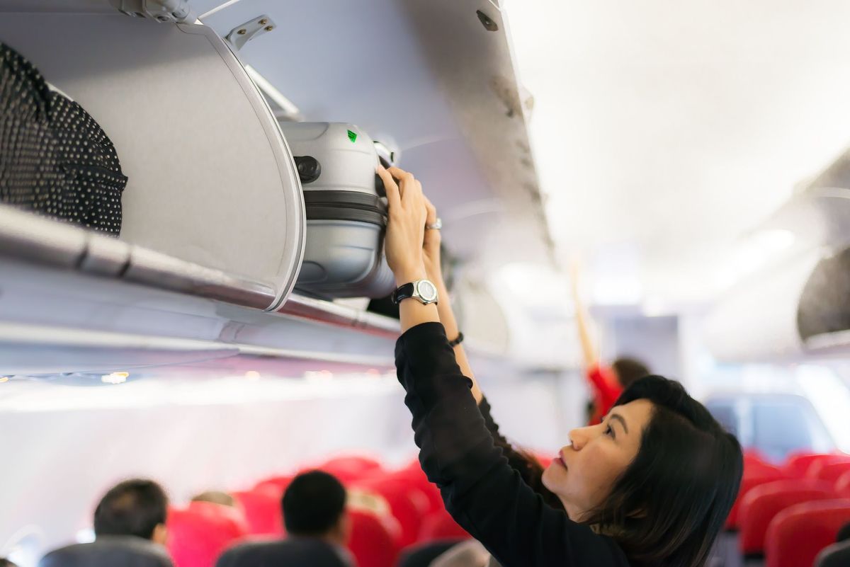 Reisende und Tourismusfrau öffnen Überkopfschließfach im Flugzeug, Handgepäckfach mit Koffern im Flugzeug. Hände nehmen Handgepäck ab. Der Passagier stellte die Kabinentaschenkabine auf das oberste Regal. Reisekonzept