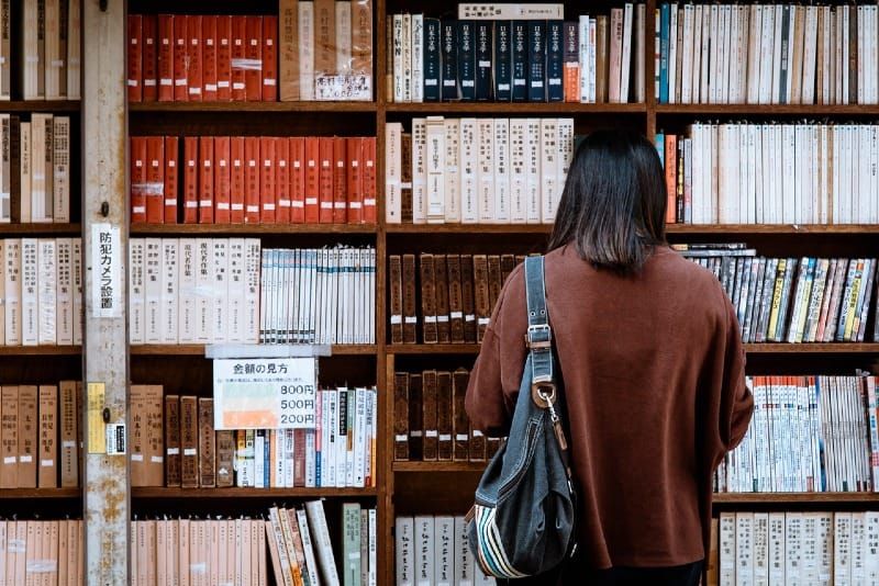 Frau im braunen Hemd, die vor Bibliotheksbüchern steht