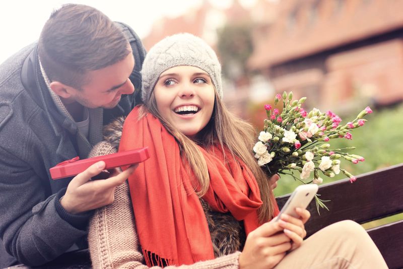 im park auf einer bank gibt ein mann einer lächelnden frau ein geschenk