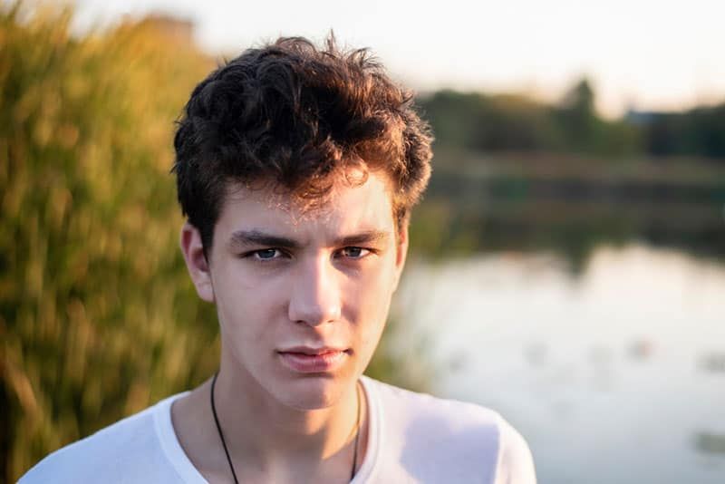 jove trist al costat del llac a la posta de sol