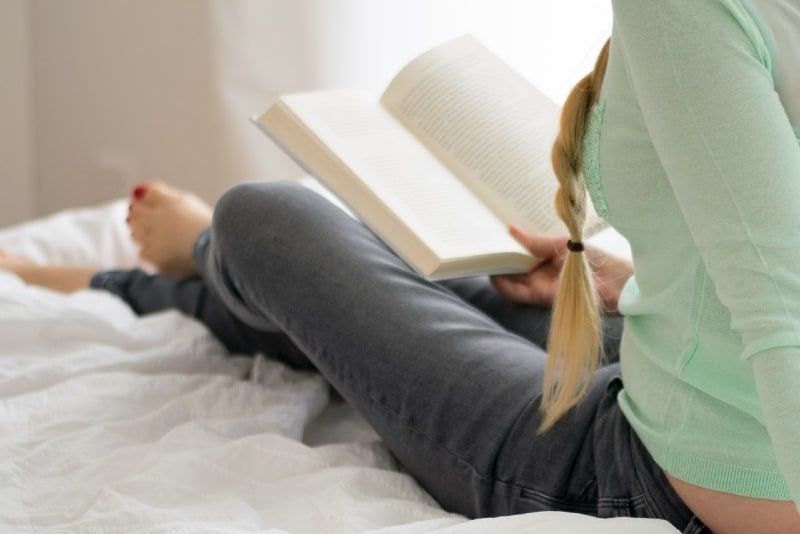 Frau liest Buch, während sie auf dem Bett sitzt