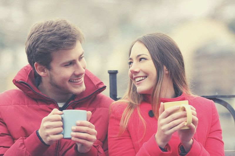 cặp đôi mặc bộ đồ mùa đông màu đỏ ngồi cạnh nhau và uống đồ uống nóng