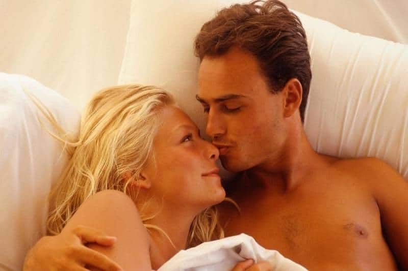 dona abraçada amb un home que la besa al llit