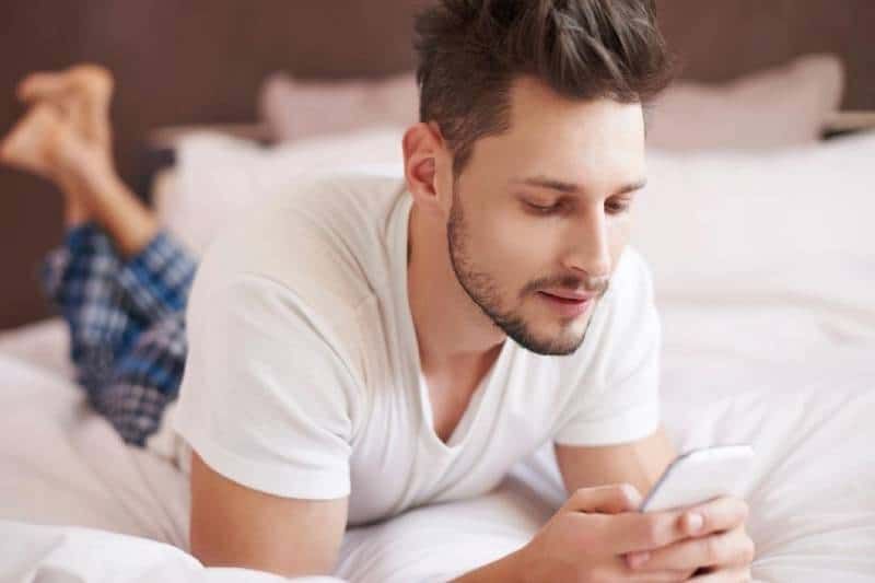 home enviant missatges de text al llit mentre portava pijama