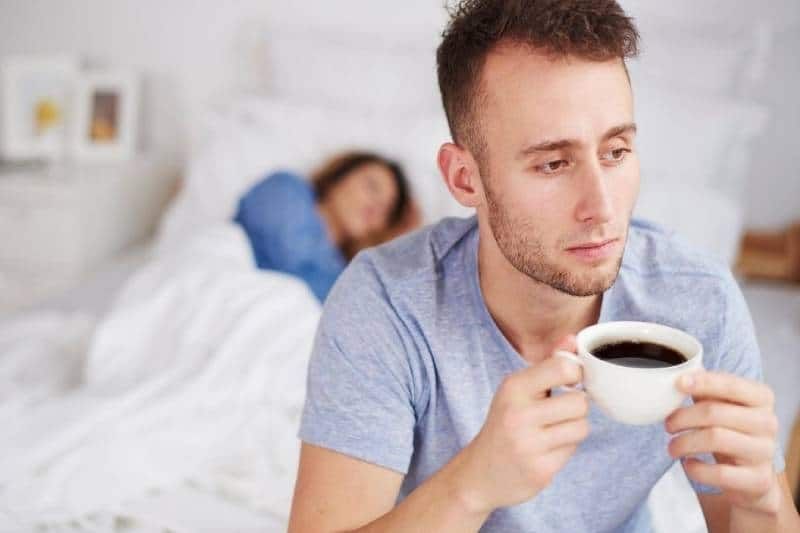 home prenent cafè al llit i una dona dormint darrere seu