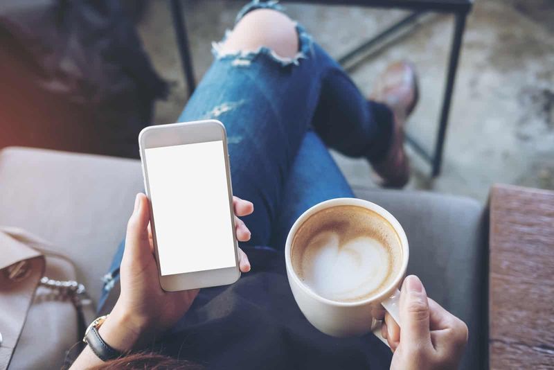 eine Frau, die ein Telefon und eine Tasse Kaffee in der Hand hält