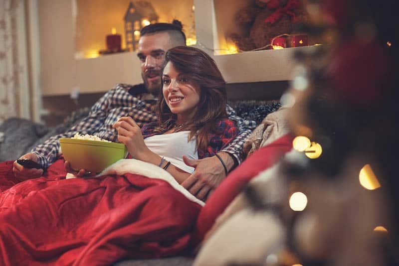 người đàn ông ôm phụ nữ khi ngồi trên ghế dài và ăn bỏng ngô