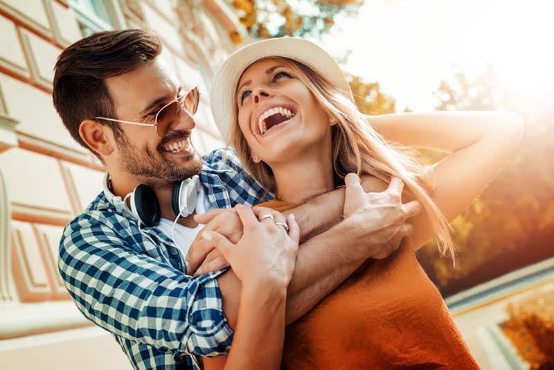 người đàn ông ôm người phụ nữ mỉm cười từ bên ngoài