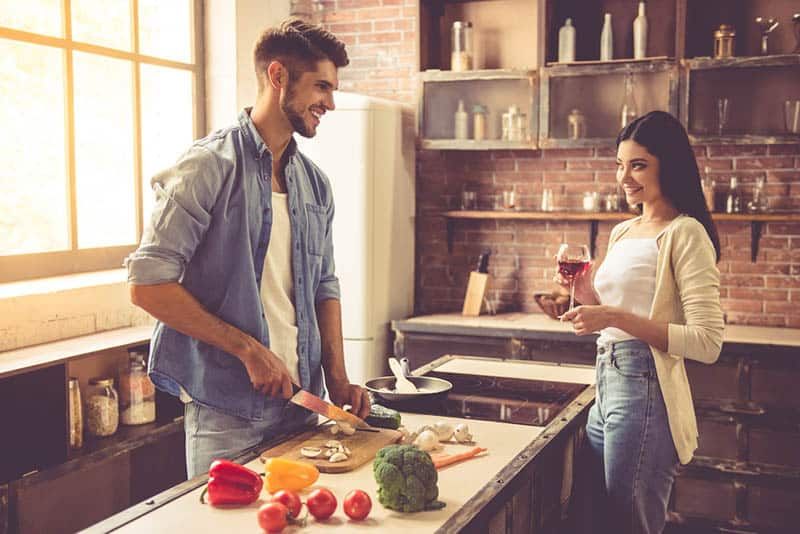 Người đàn ông mỉm cười cắt nấm bằng dao trong nhà bếp và nhìn vào người phụ nữ
