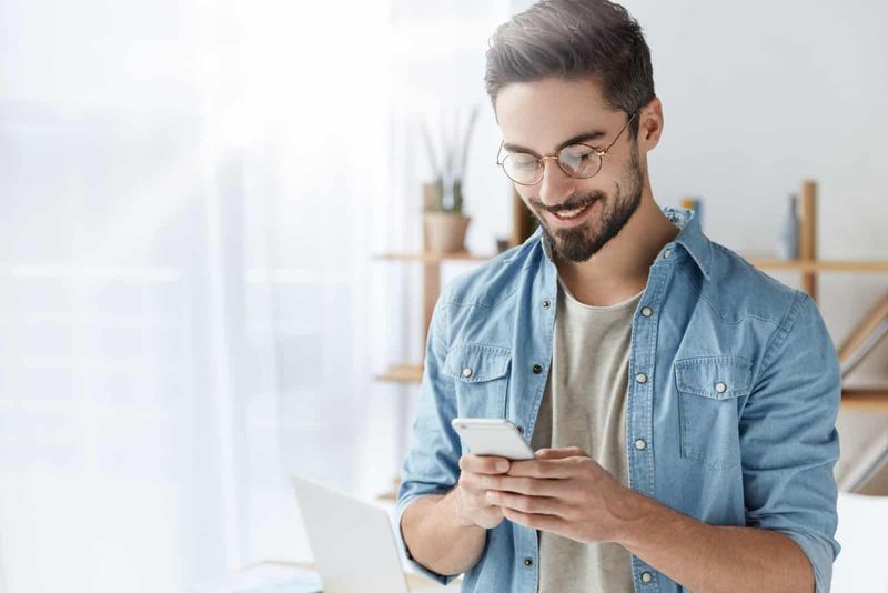 uśmiechnięty mężczyzna w okularach piszący na telefonie komórkowym