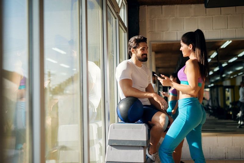 formet sporty pige, der flirter med en fyr i gymnastiksalen med en smartphone