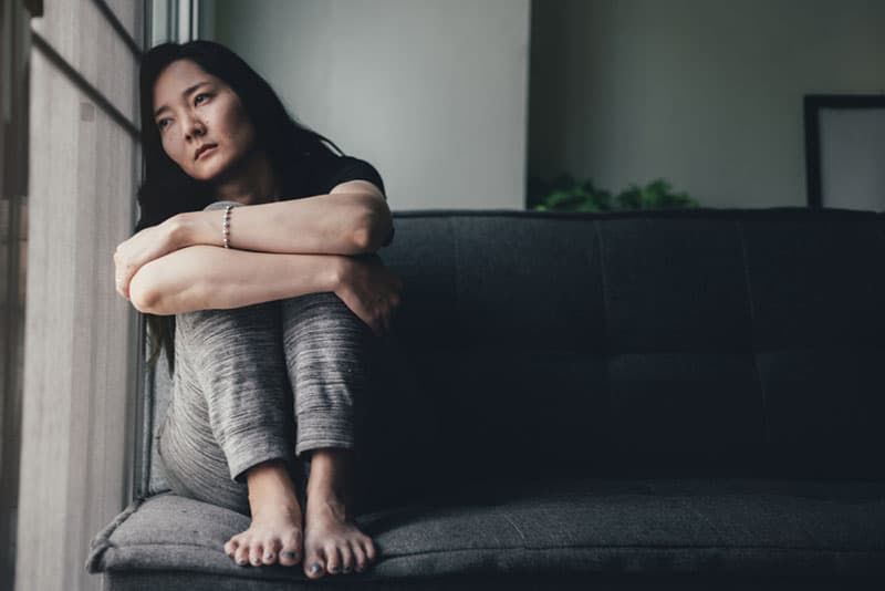 Trauriges chinesisches Mädchen, das neben dem Fenster sitzt