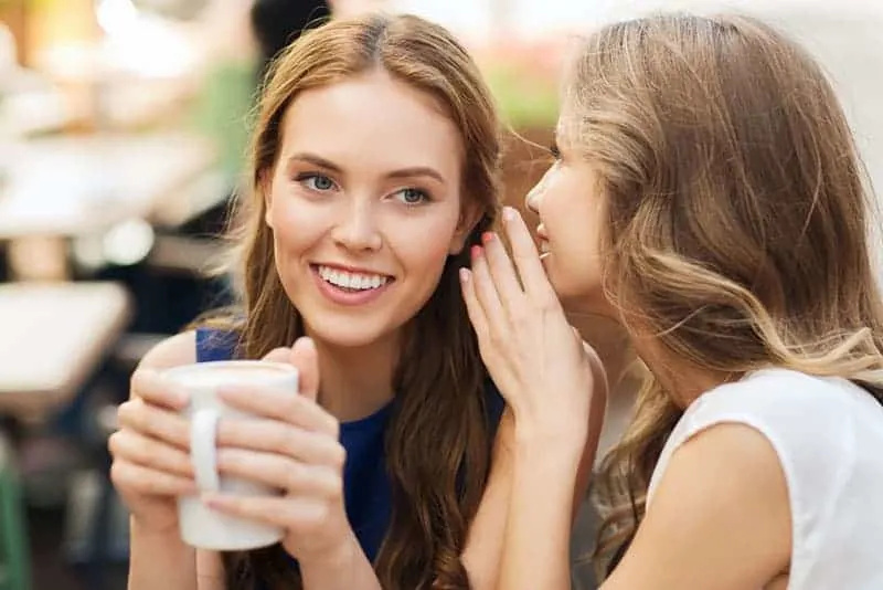  Lächelnde junge Frauen trinken Kaffee oder Tee und tratschen in einem Straßencafé'aperto