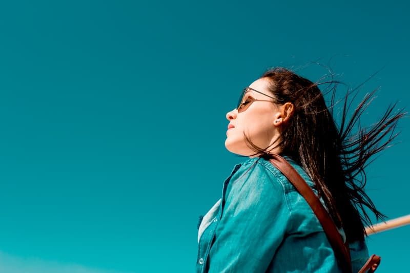 wanita mengenakan atasan biru dan kacamata hitam menatap langit biru