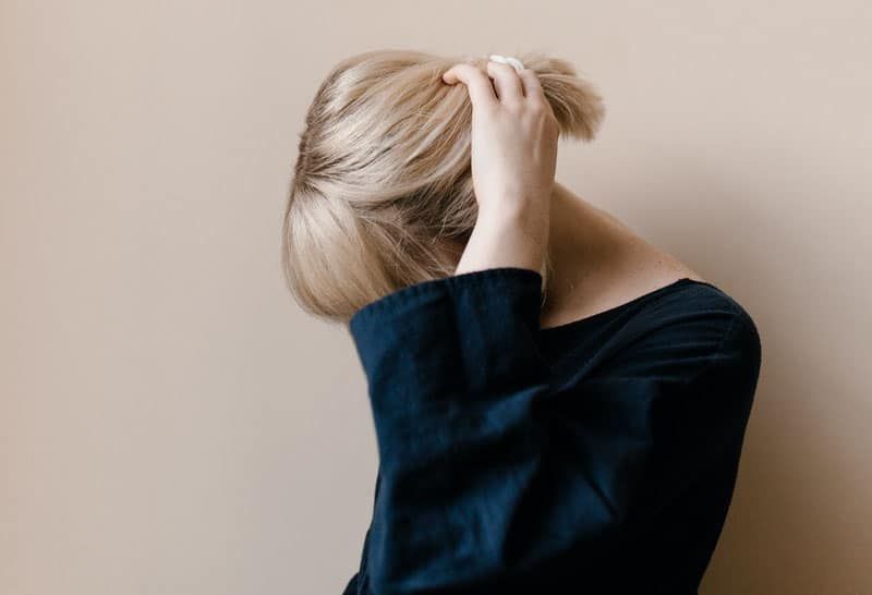 wanita dengan rambut pirang di atas biru memegang rambutnya