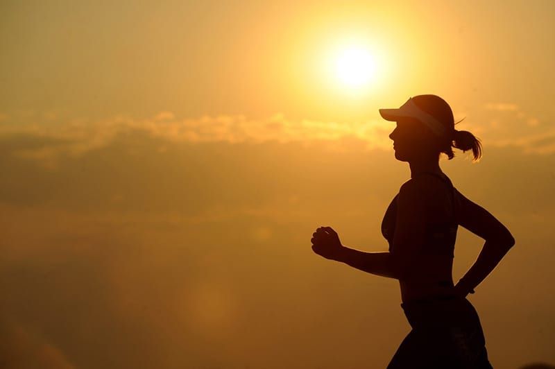 Silhouet van rennende vrouw met zonsondergangachtergrond