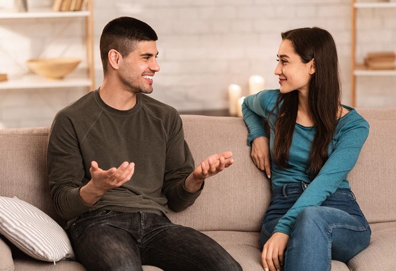 رجل مبتسم يتحدث مع صديقته أثناء جلوسه على الأريكة