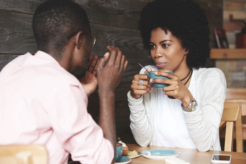 uma mulher com cabelos crespos bebe café e conversa com um homem