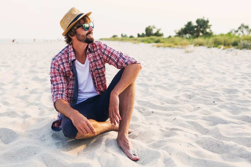 uśmiechnięty mężczyzna w kapeluszu na głowie siedzi na plaży