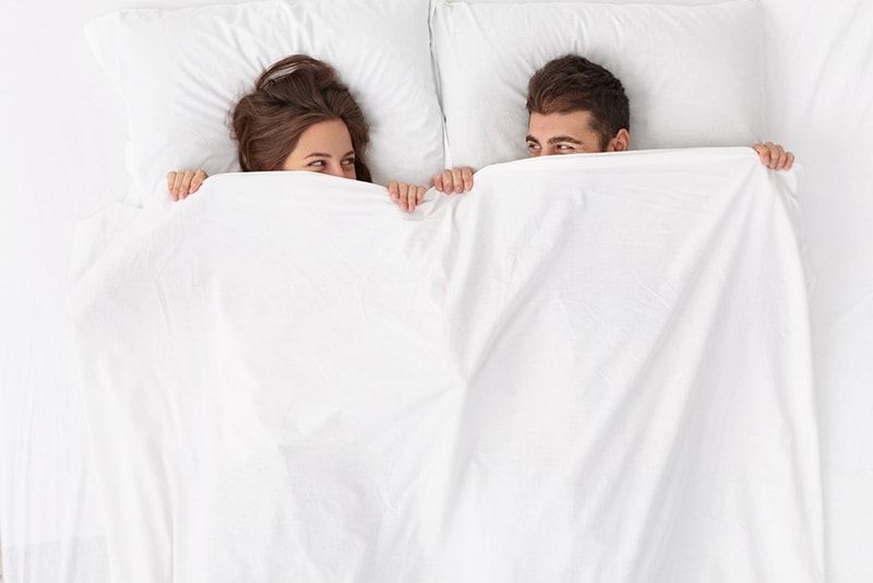 cặp đôi nằm trên giường trải khăn trắng và nhìn nhau
