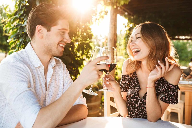 uśmiechnięty mężczyzna i kobieta rozmawiają i wznoszą toast winem
