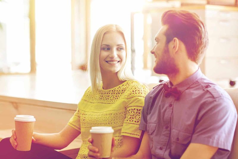 uśmiechnięta blond kobieta pije kawę i rozmawia z mężczyzną