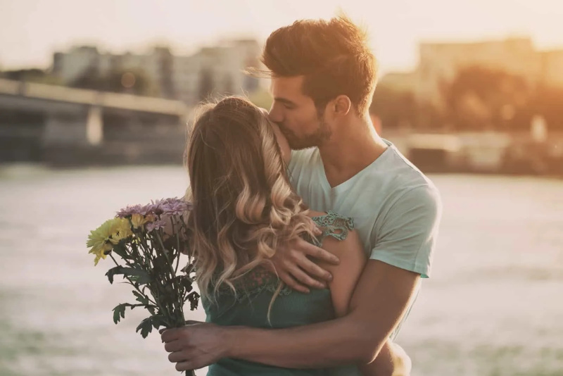   home sostenint un ram de flors mentre besa a una dona
