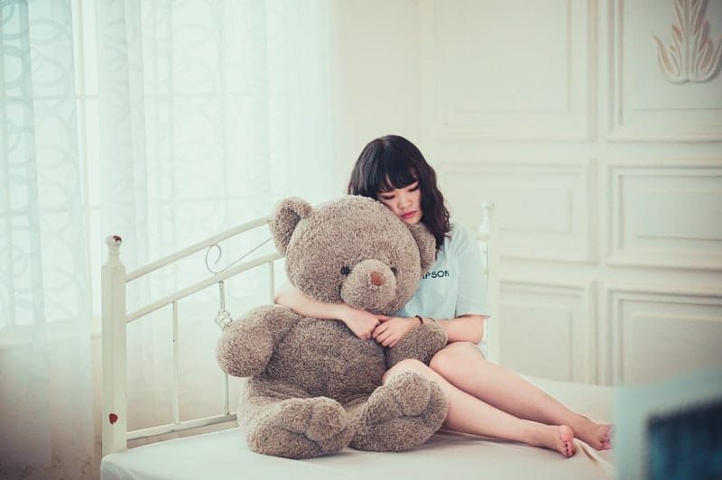 wanita dewasa di tempat tidur memeluk boneka beruang besar