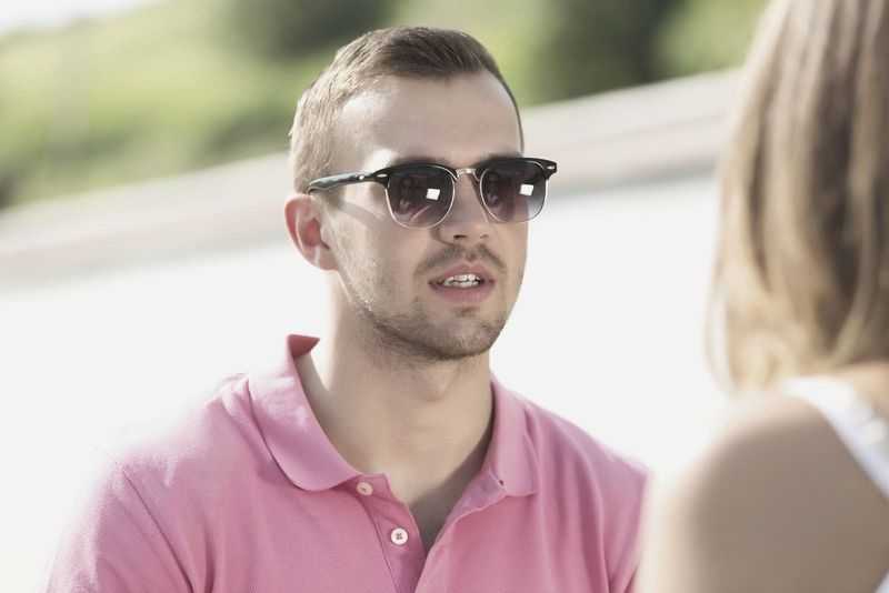 knappe jonge man met roze top en zonnebril in gesprek met een vrouw buitenshuis