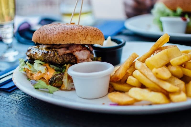 burger si cartofi prajiti asezati intr-o farfurie alba cu recipient cu sos