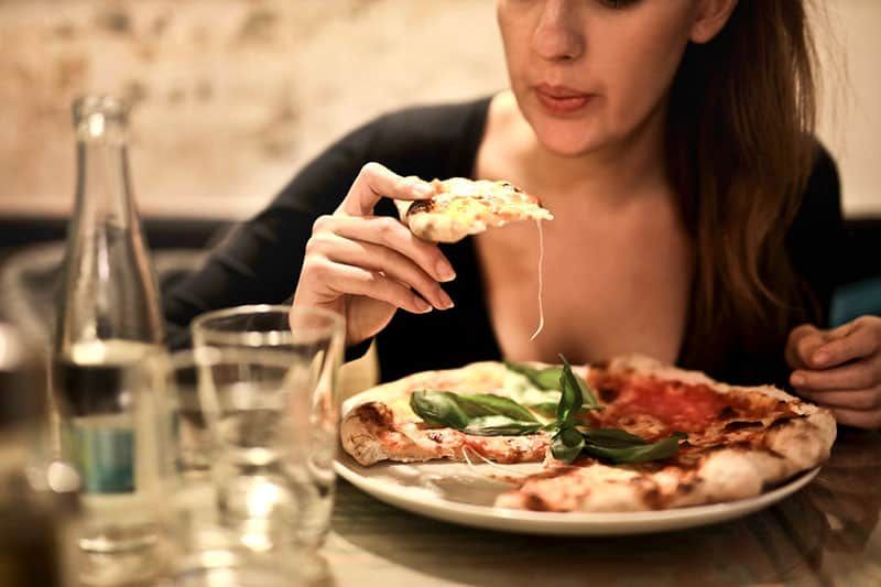 femeie ține pizza feliată lângă masă cu pahar