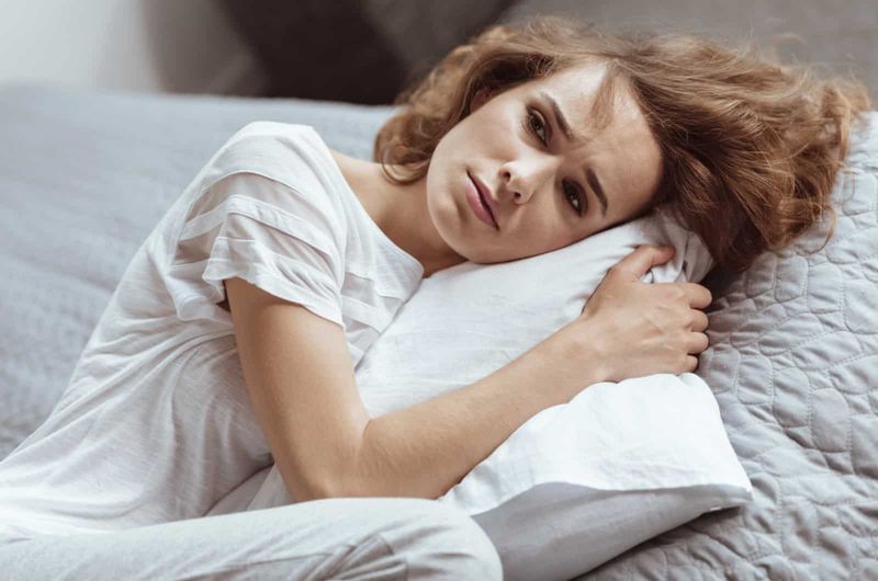 người phụ nữ lo lắng ôm gối trong nhà