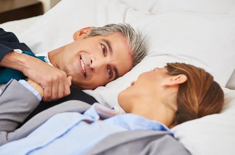 pria dan wanita yang lebih tua berbaring di tempat tidur dengan setelan kantor mereka