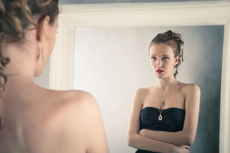 امرأة حزينة تنظر إلى المرآة ترتدي فستانًا أسود