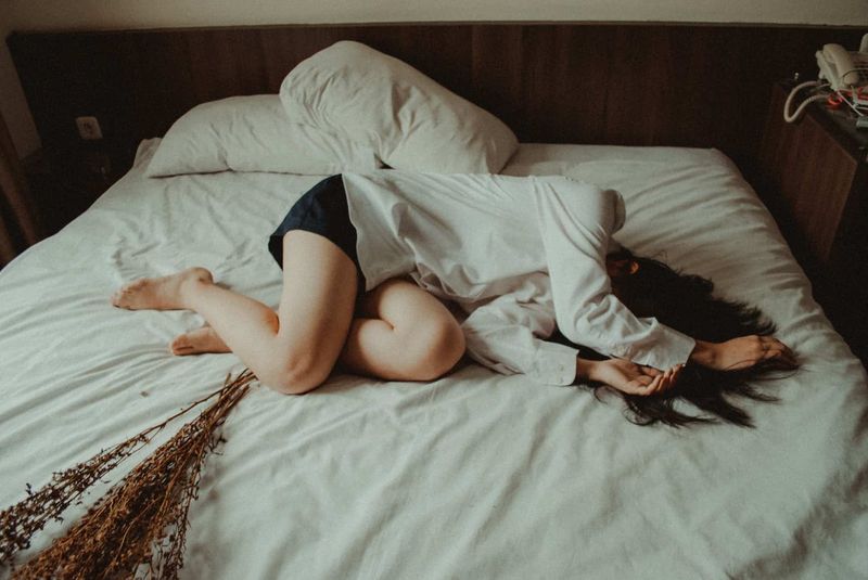 người phụ nữ nằm bên cạnh những bông hoa khô mặc áo dài trắng và che mặt