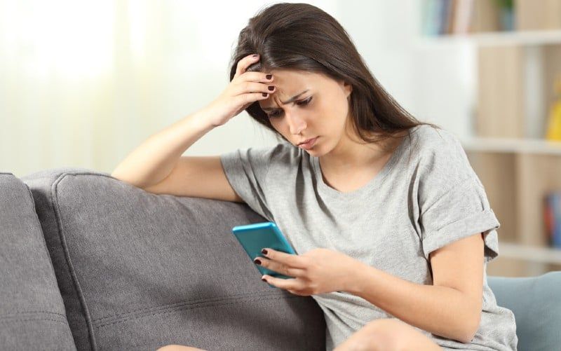 Verdrietig meisje met smartphone in de ene hand zittend op een bank