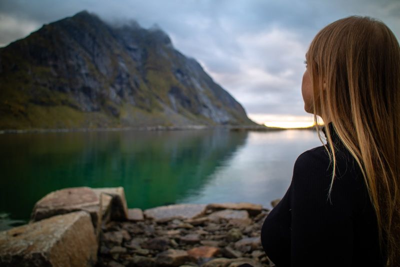 vrouw in zwarte coltrui die bij het meer zit