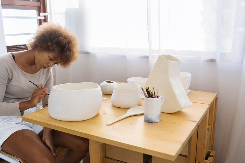 vrouw die een keramische kom schildert terwijl ze aan tafel zit