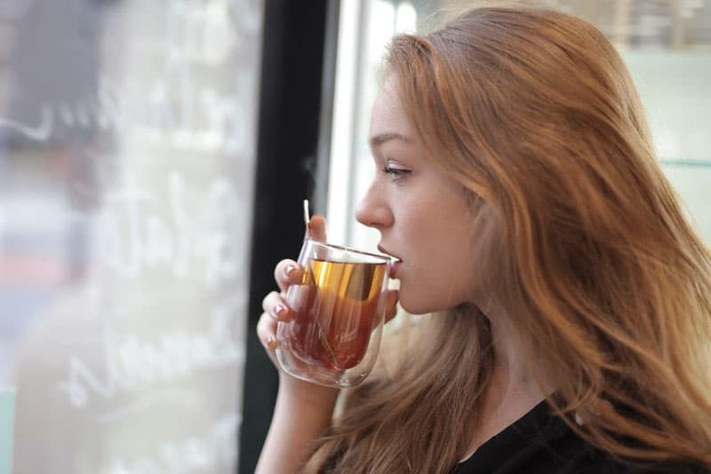 Frau im Begriff, Tee aus einer Tasse in der Nähe der Fenster zu trinken