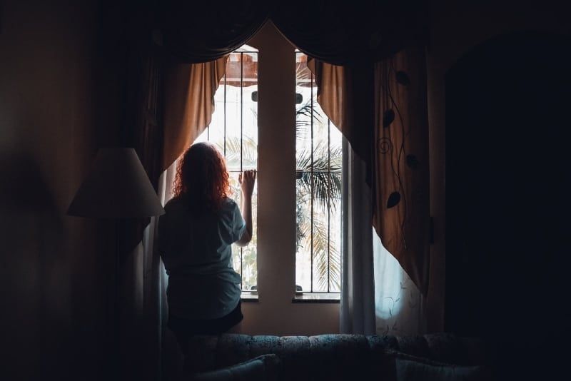 vrouw die bij het raam staat en door het raam kijkt