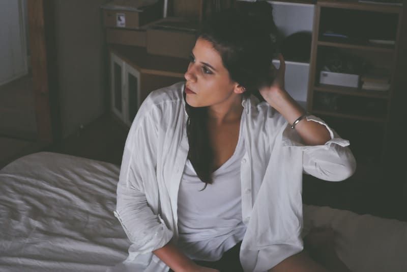 vrouw die haar haar aanraakt terwijl ze op bed zit